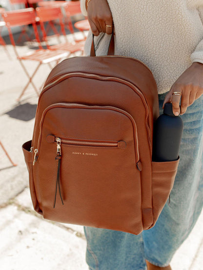 Brown backpack held by a person with a blurred outdoor background