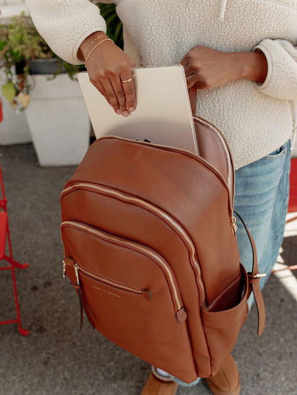 Person placing a laptop into a brown vegan leather backpack